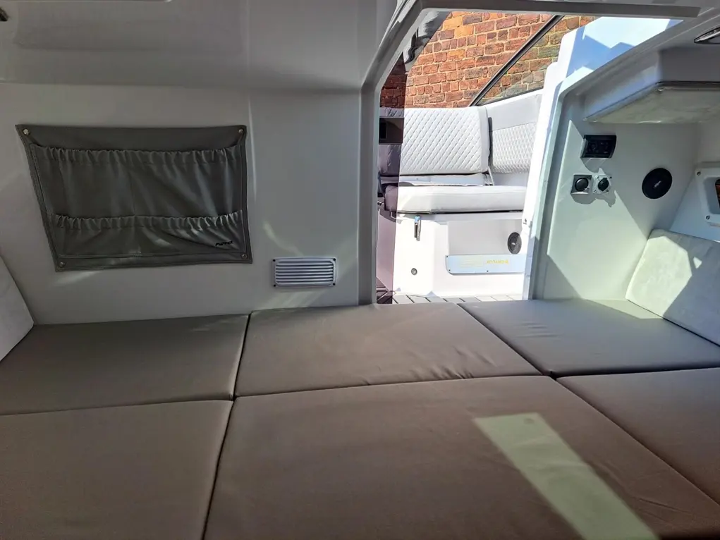 Interior of a boat showing a grey linen storage pocket, along with a seating area and control panel in bright lighting.